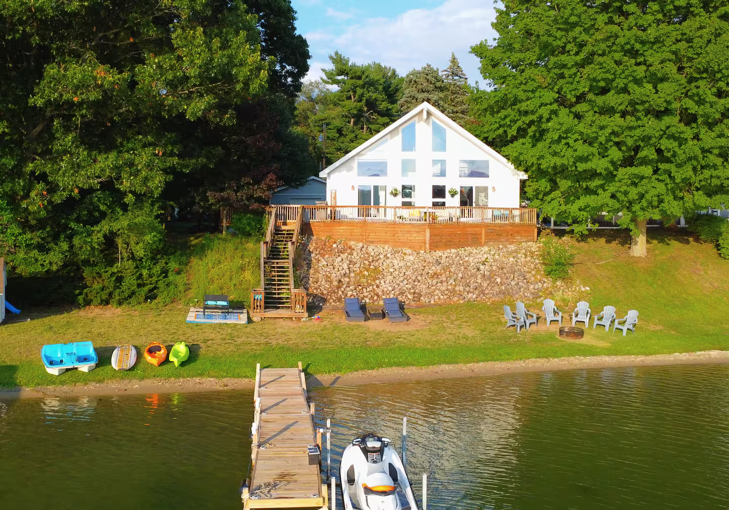 Aerial view of Casa Estiva, a white gabled lakehouse with a private dock and sandy beach on Big Twin Lake